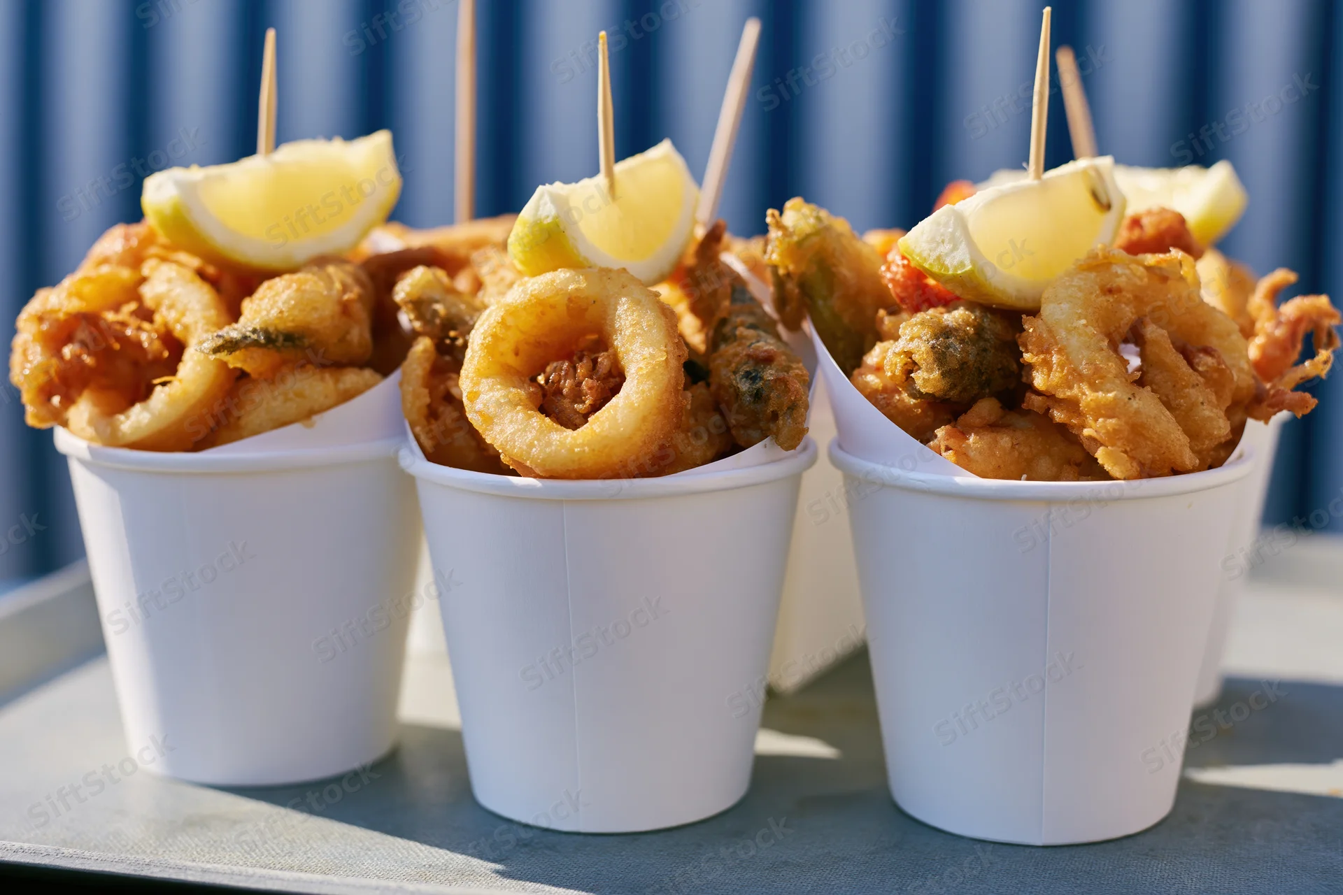 Fried seafood in white paper cups with lemon wedges on a tray outdoors