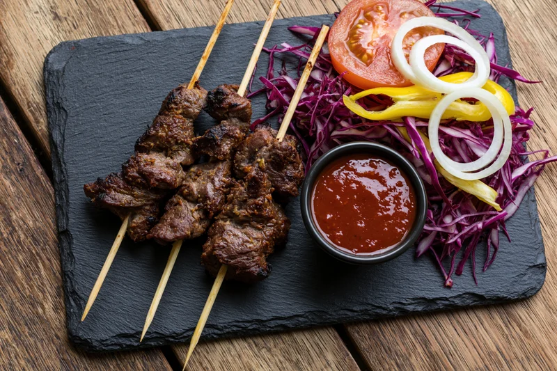 Grilled meat skewers with vegetable salad and sauce on slate plate