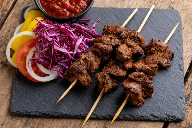 Grilled meat skewers with vegetables and sauce on a slate plate