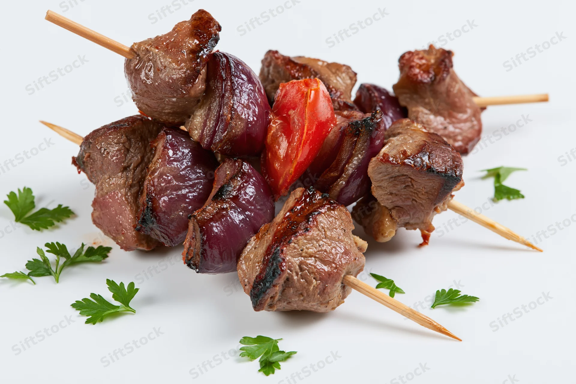 Grilled beef kebabs with red pepper and onion on wooden skewers, garnished with parsley, arranged on white background