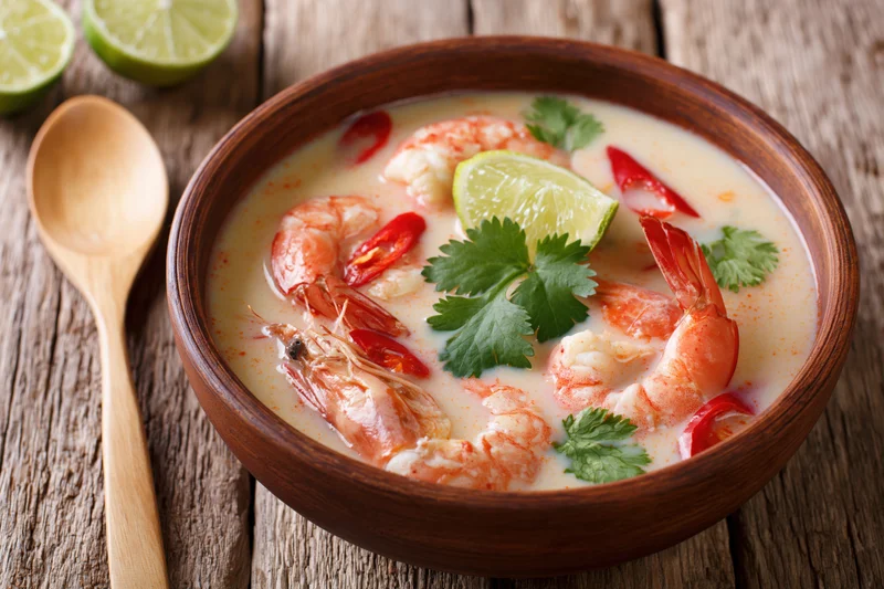 Tom kha gai soup with shrimp and lime in a wooden bowl on a rustic table