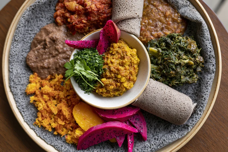 Traditional ethiopian injera platter with stews and vegetables arranged on a gray ceramic plate viewed from above