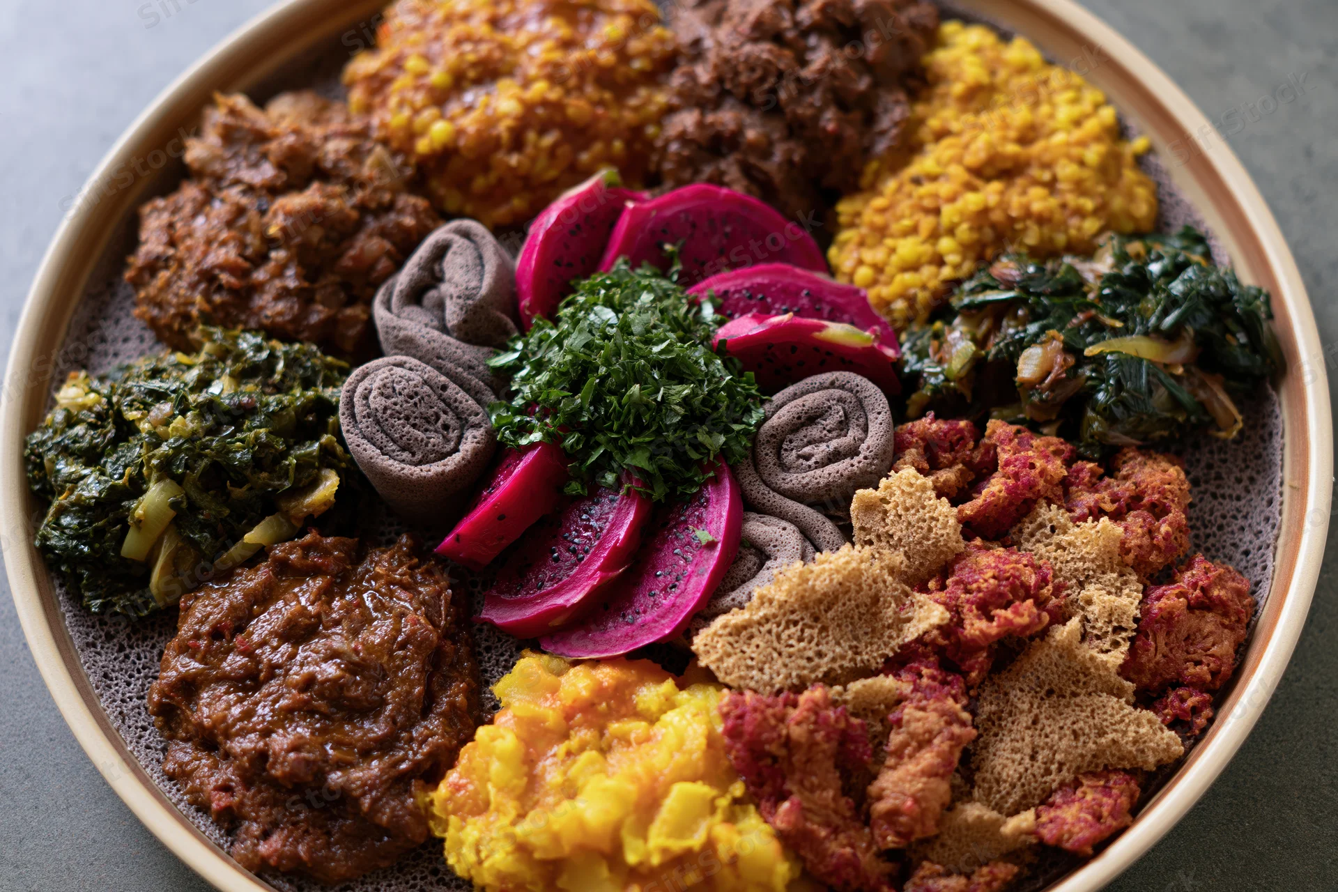 Traditional ethiopian injera platter with stews vegetables and legumes arranged on a round plate viewed from above
