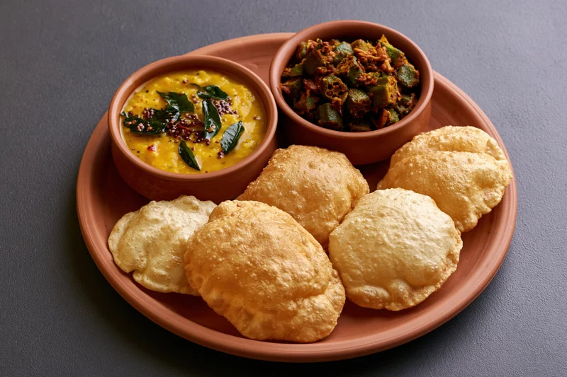 Traditional indian meal with samosas, dal, and okra curry served on a terracotta clay platter