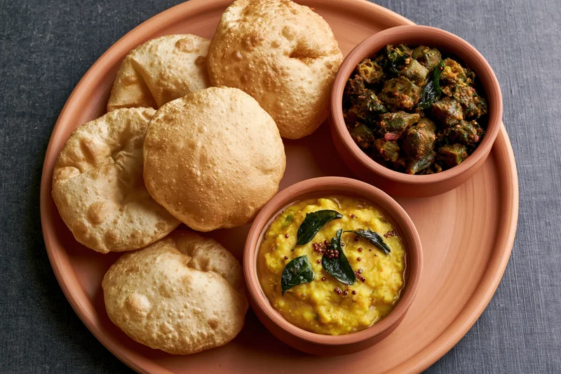 Traditional indian meal with puri bread, dal, and vegetable curry served on a round terracotta platter