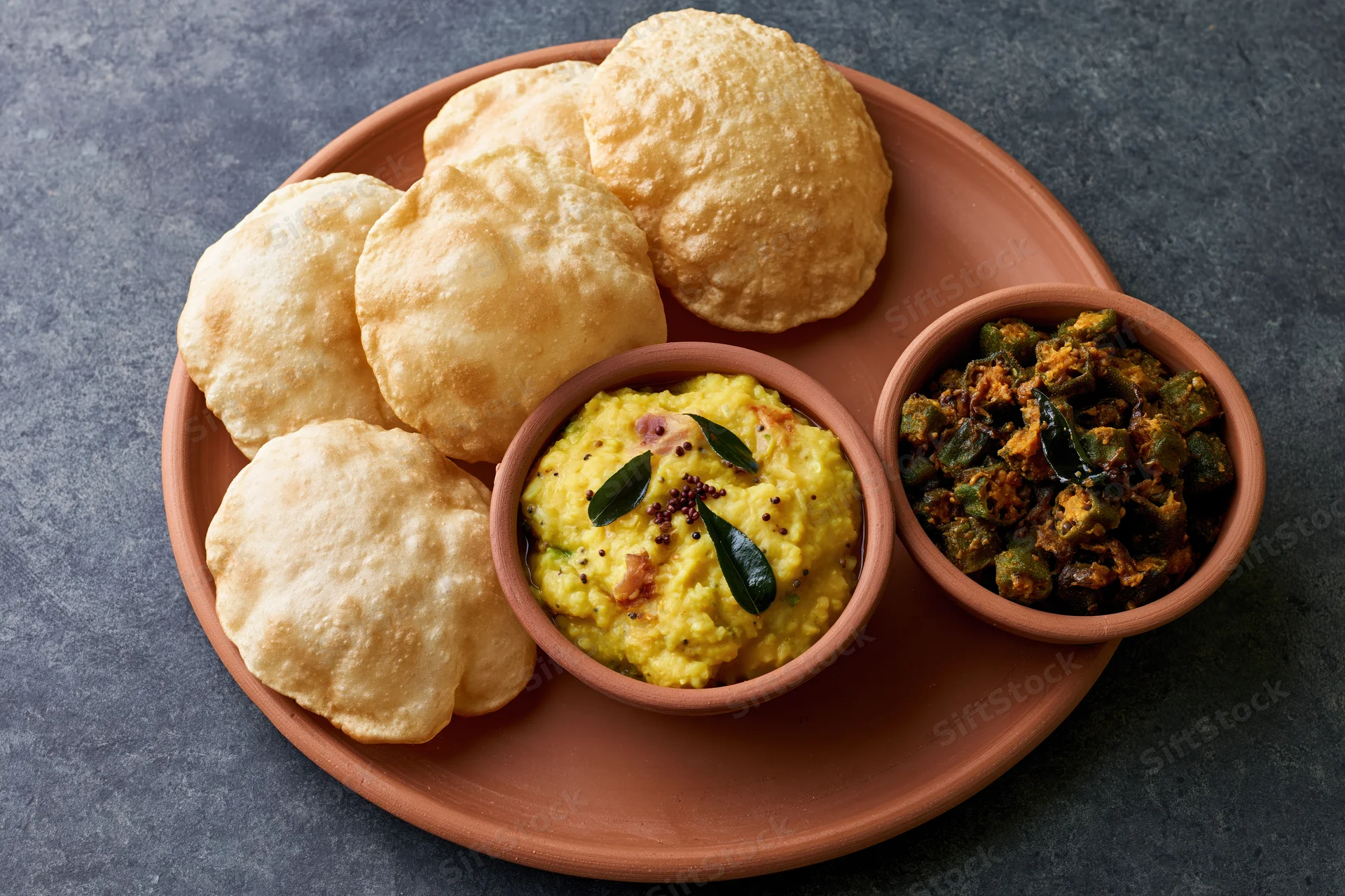 Traditional indian meal with puri, dal, and okra curry served on terracotta platter