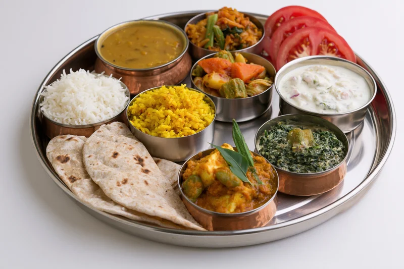 Traditional indian thali meal served on a stainless steel plate with rice, curry, dal, raita, and roti