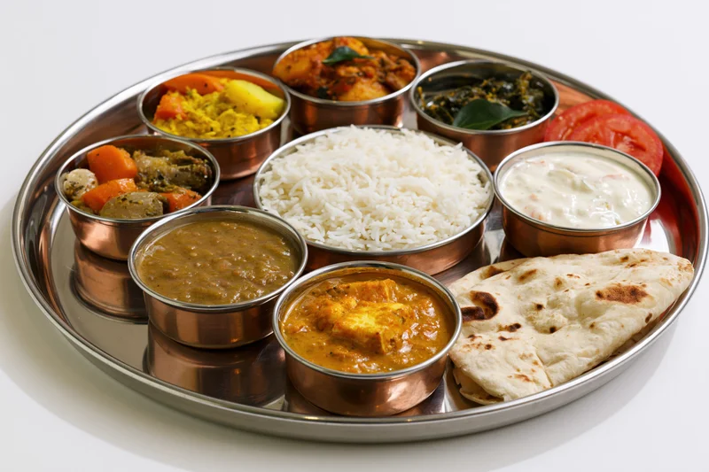 Traditional indian thali meal with rice, curries, naan and yogurt on a metal tray