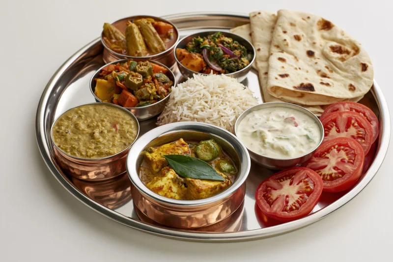 Traditional indian thali meal served on a stainless steel tray with copper bowls and flatbread