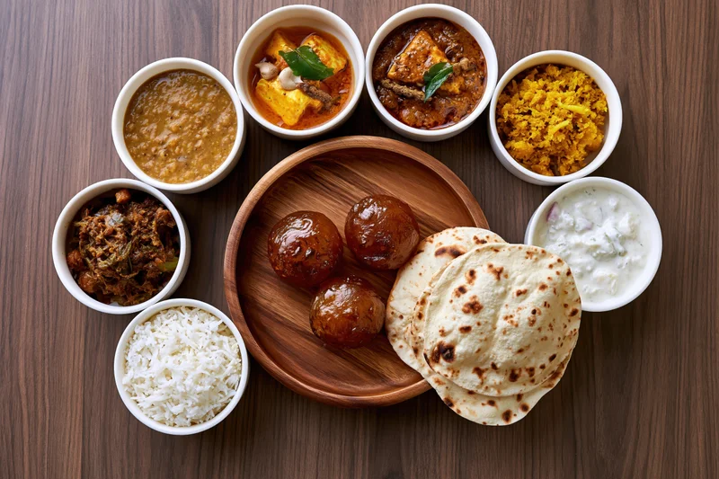 Traditional indian thali spread with curries, rice, roti and sweets arranged on a wooden tray