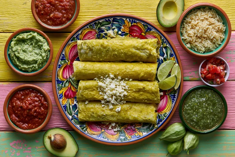 Traditional mexican enchiladas verdes served on a colorful talavera plate with side dishes on a painted wooden table