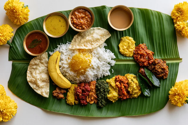 Traditional south indian onam sadya meal served on banana leaf with rice, curries, papad, banana, and marigold flowers around