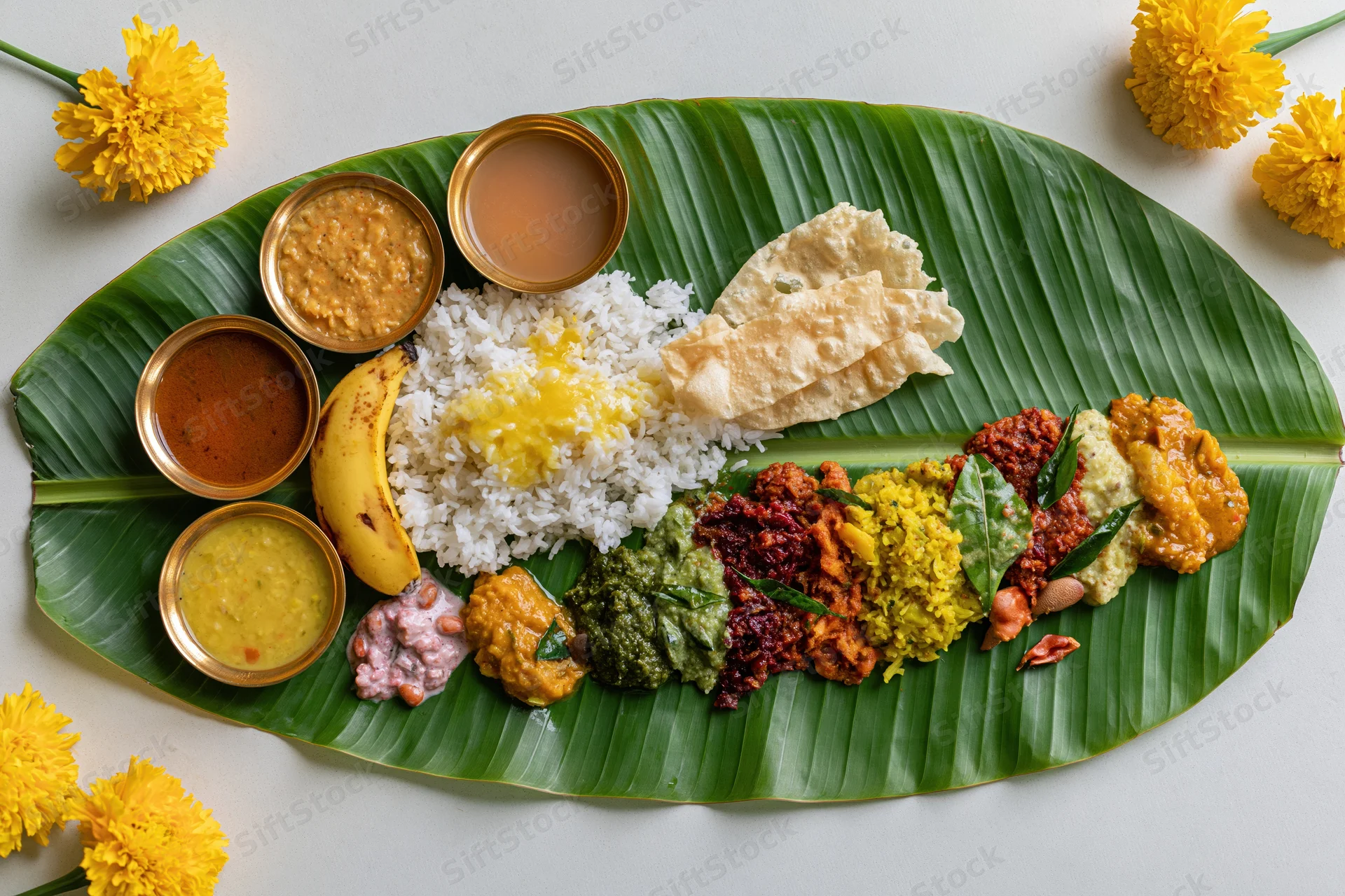 Traditional south indian onam sadya meal served on banana leaf with rice, curries, sweets and marigold flowers around