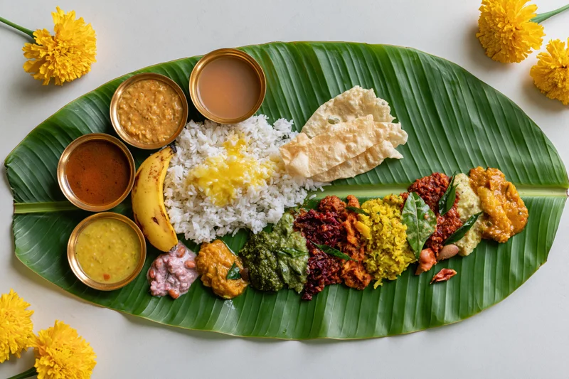 Traditional south indian onam sadya meal served on banana leaf with rice, curries, sweets and marigold flowers around