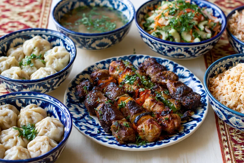 Traditional uzbeck feast with kebabs, dumplings, rice, soup and salad served on patterned tablecloth