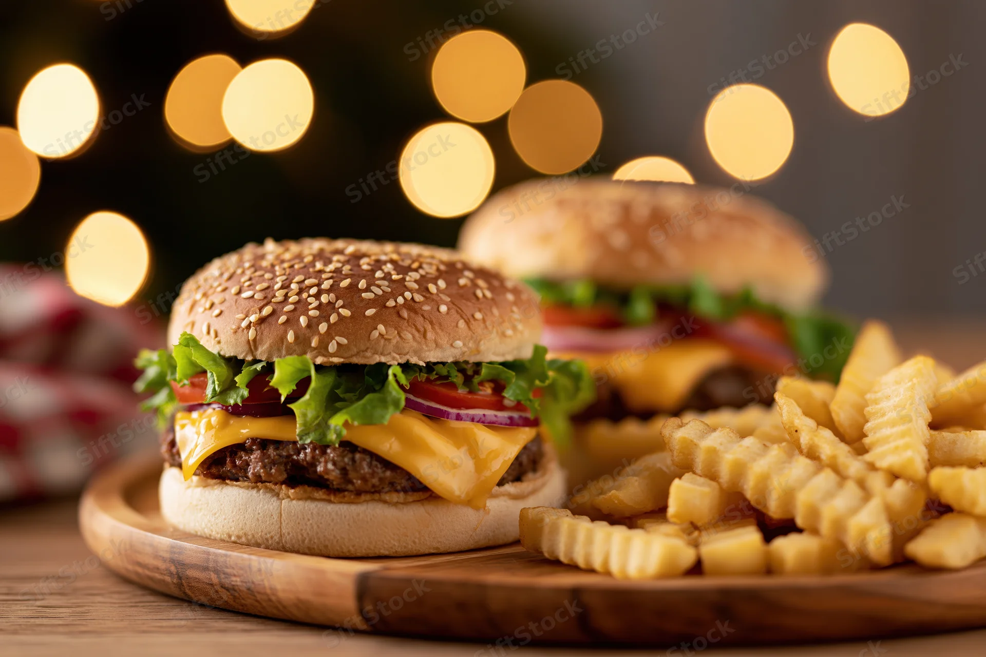 Two cheeseburgers with sesame seed buns and crinkle-cut fries on a wooden plate with blurred festive lights in the background