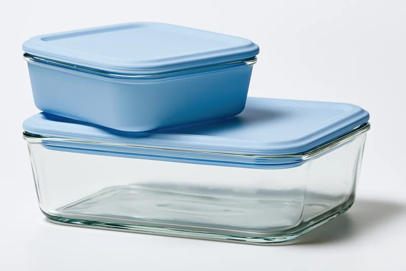 Two clear glass food storage containers with sky-blue plastic lids stacked on white background
