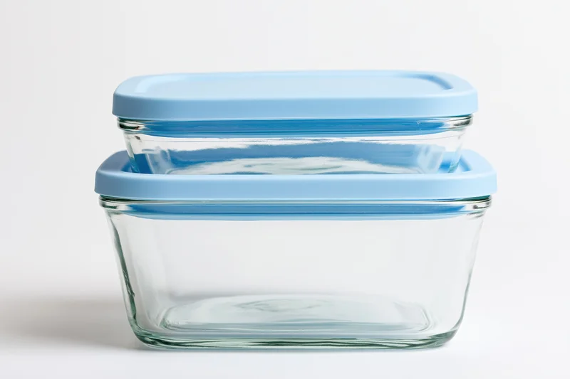 Two clear glass food storage containers with sky-blue plastic lids stacked on a white surface