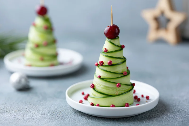 Cucumber ribbon christmas tree appetizers on small white plates with cranberry garnish and star decoration