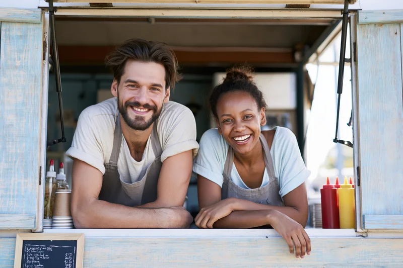 Two food truck workers, a young man and woman leaning together