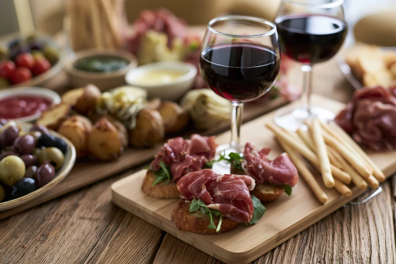 Two glasses of red wine on a wooden board with charcuterie and appetizers arranged for a gathering