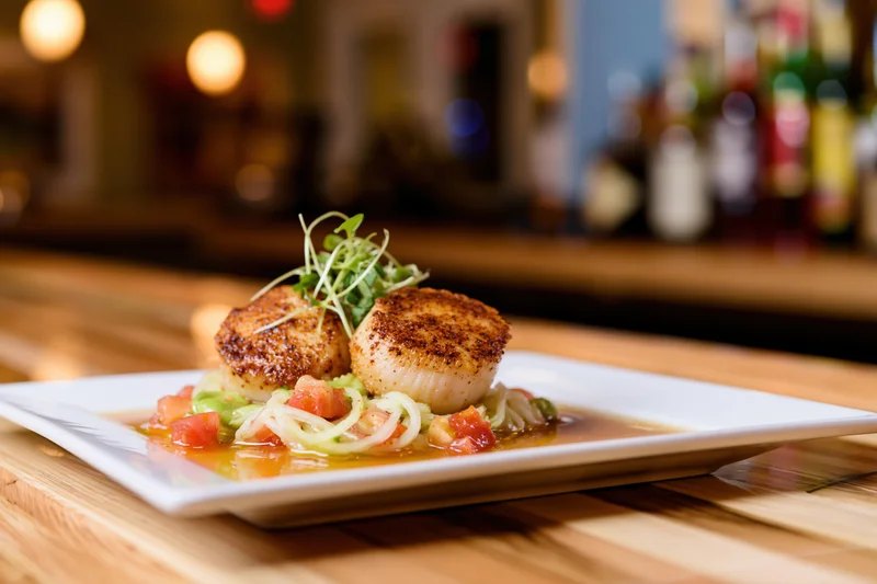 Seared scallops with tomato onion sauce and microgreens on white plate on wooden table in restaurant