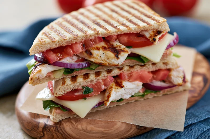 Two grilled panini sandwiches stacked on a wooden olive board