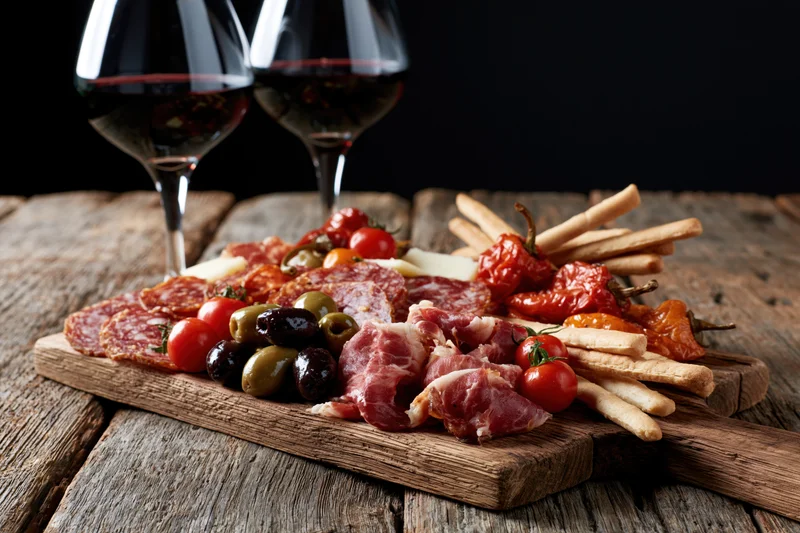 Two wine glasses with red wine beside a charcuterie board on a wooden table
