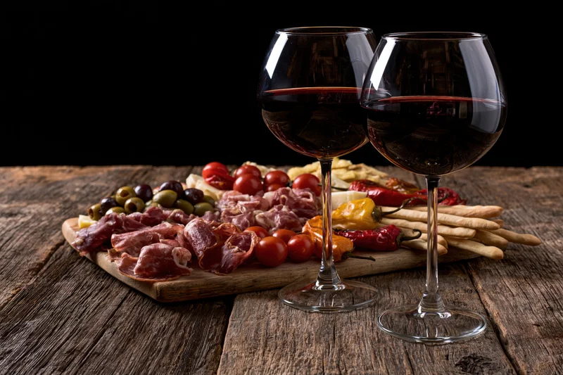 Two wine glasses with red wine in front of a charcuterie board on a wooden table
