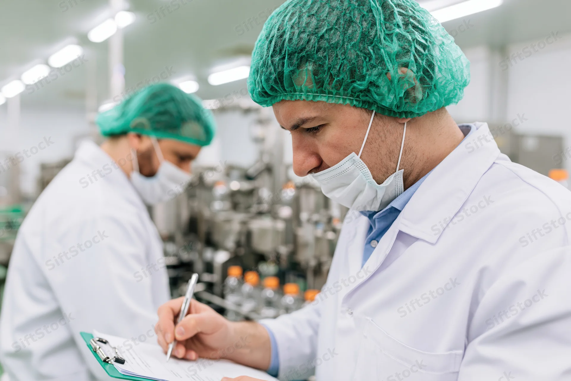 Male quality control inspector writing on clipboard in factory production area