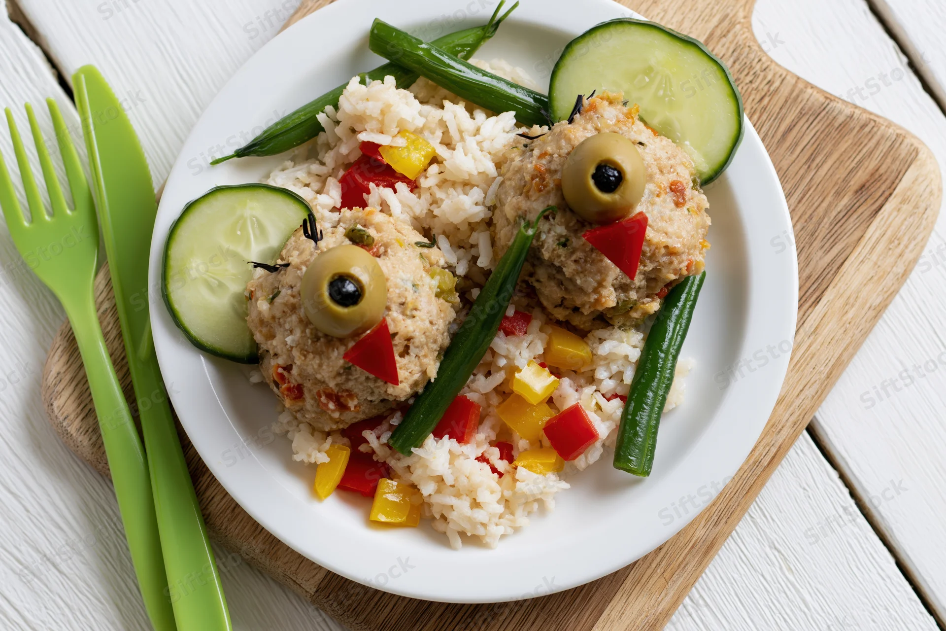 Two meatball chicks arranged as playful bird shapes on a white plate with rice and vegetables on a wooden cutting board