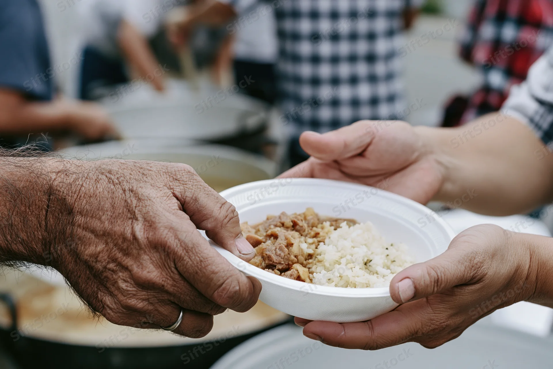Weathered hands exchanging a white styrofoam bowl of rice and meat at a food charity event
