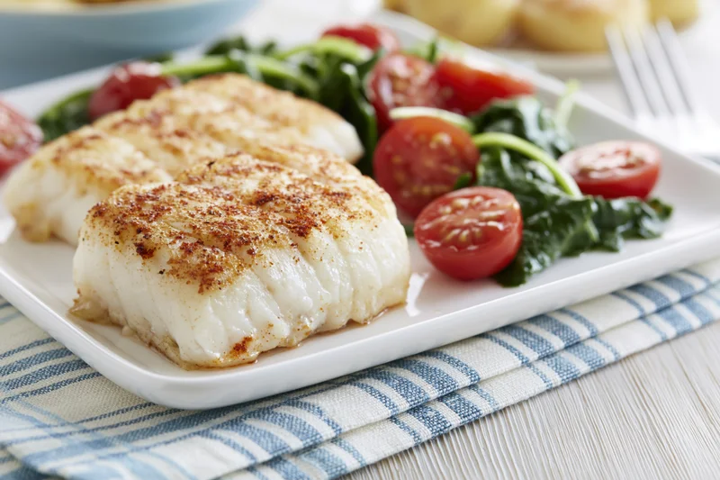 Two seared white fish fillets with cherry tomato salad on a white plate