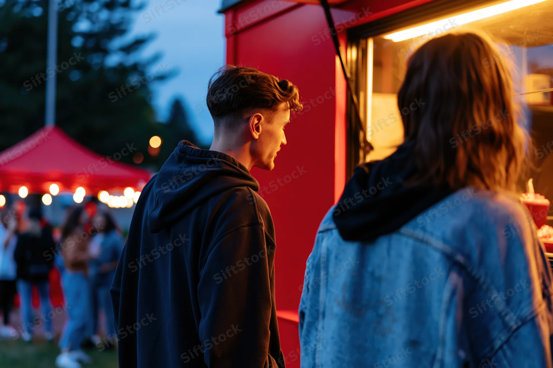 Two people ordering at a red food truck window at dusk