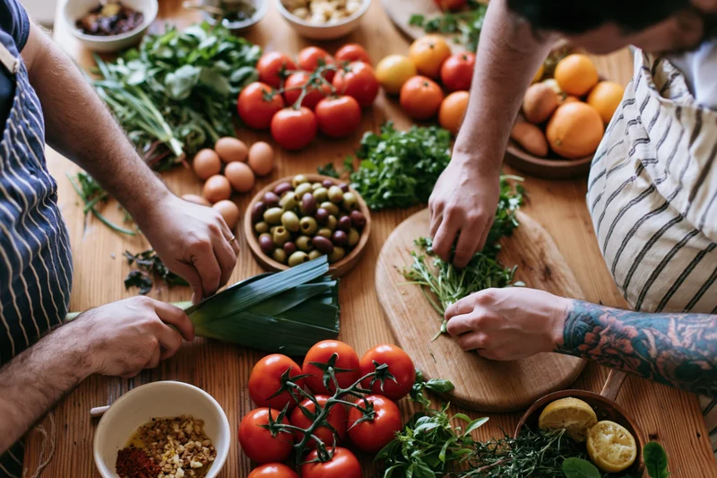 Two people chopping vegetables together on a wooden kitchen table