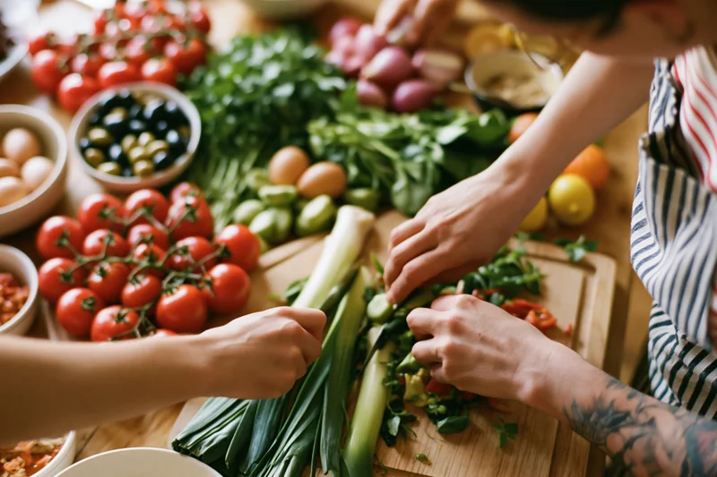 Two people chopping leeks and vegetables on a wooden cutting board in a kitchen