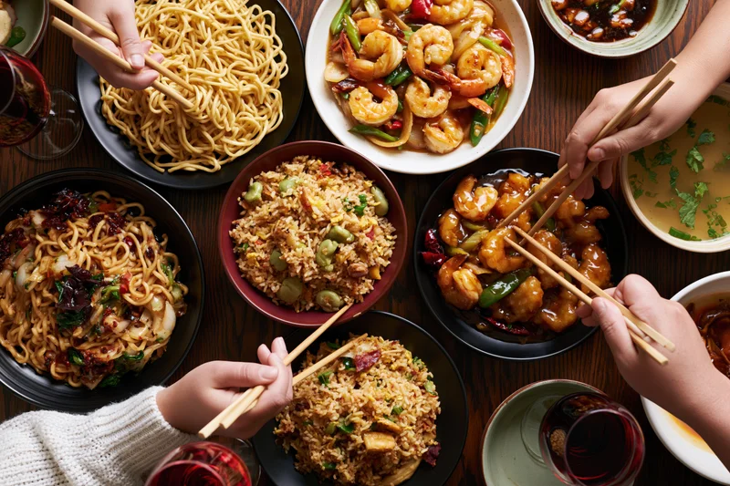 People sharing chinese dishes with chopsticks at a wooden table