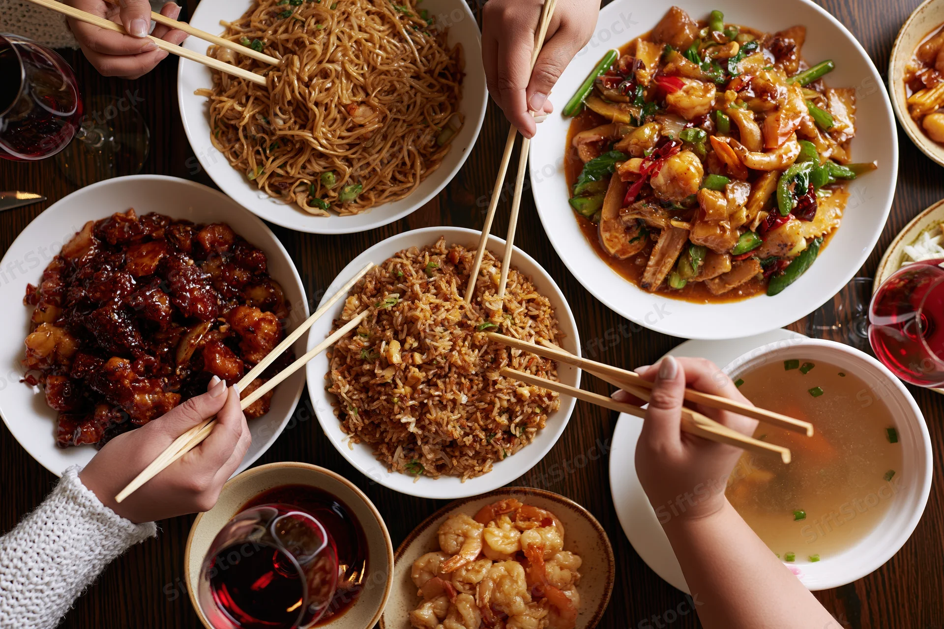 People sharing chinese dishes with chopsticks at a crowded dinner table