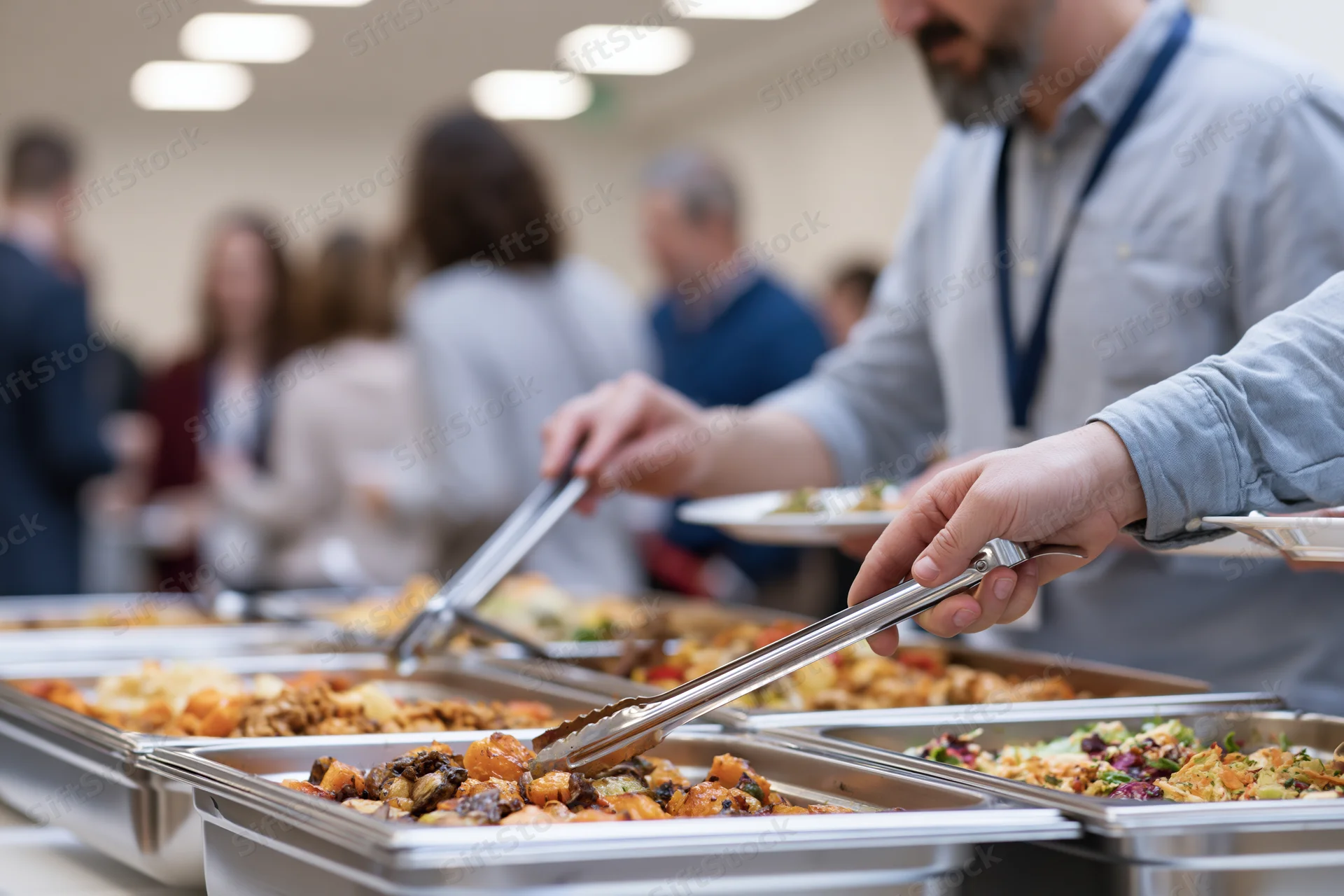 People serving themselves from a stainless steel buffet tray line in a conference room