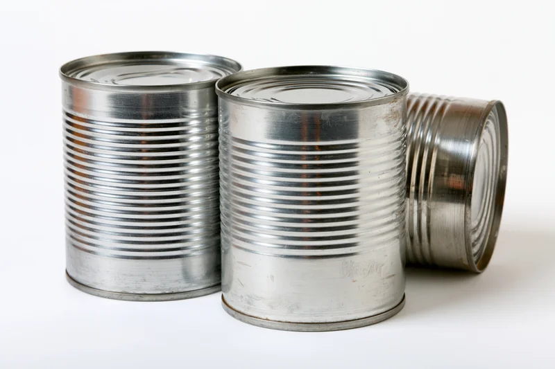 Three plain metal tin cans arranged together on a white surface