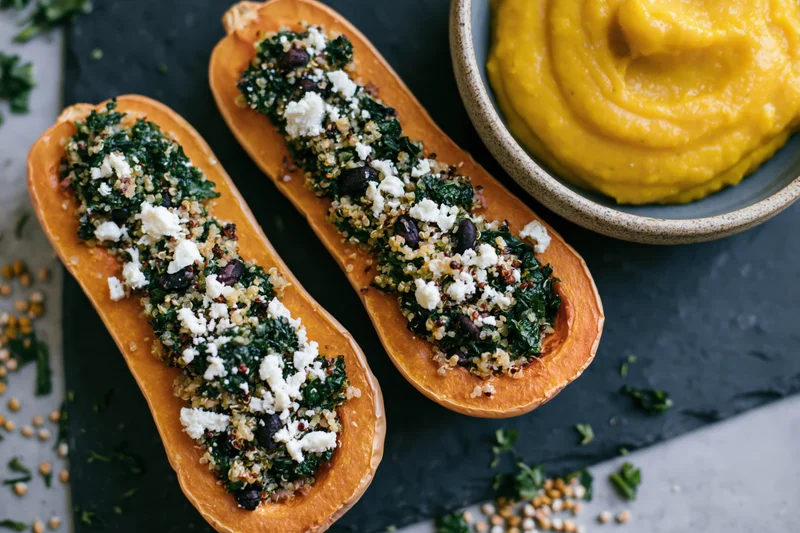 Two roasted butternut squash halves stuffed with quinoa kale and feta on a slate platter