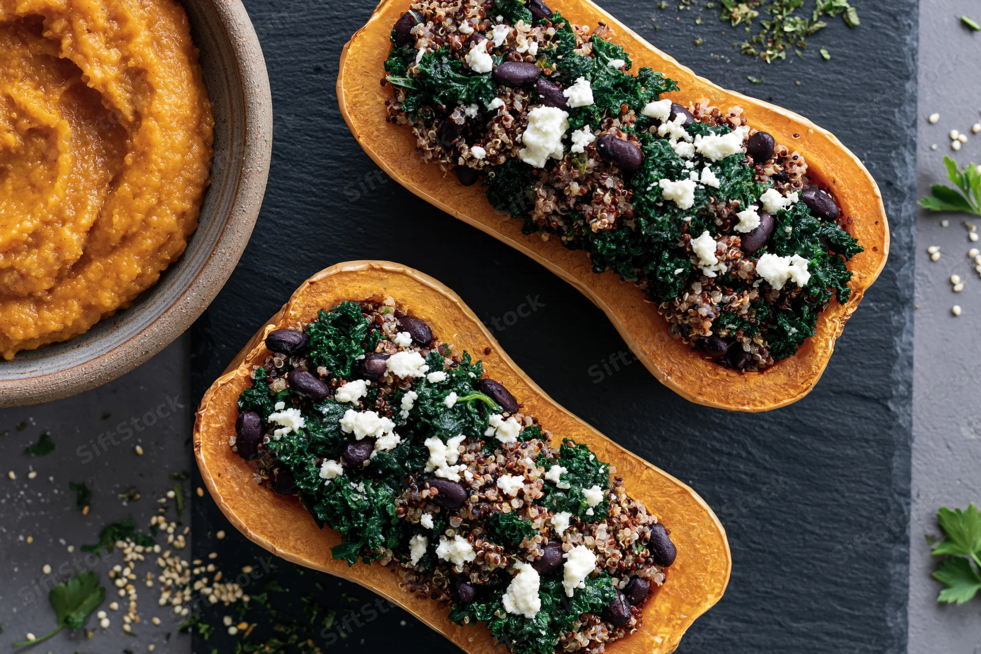 Two roasted butternut squash halves stuffed with quinoa kale and beans on a dark slate surface