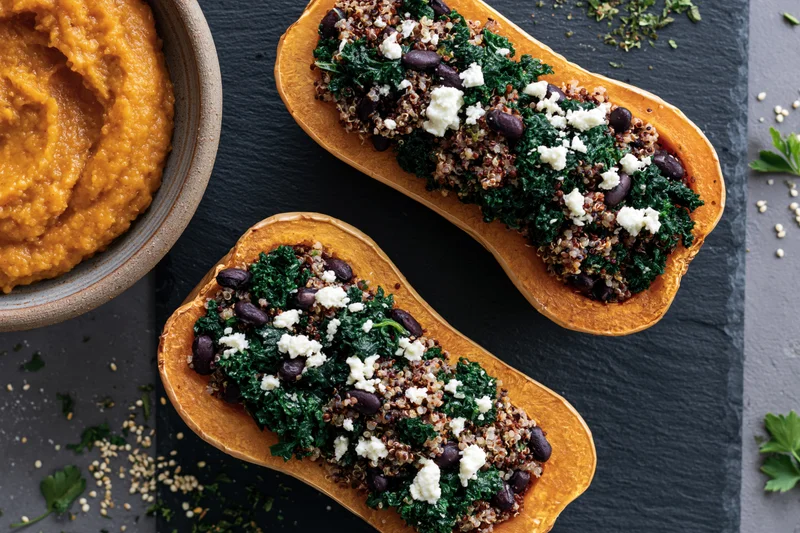 Two roasted butternut squash halves stuffed with quinoa kale and beans on a dark slate surface