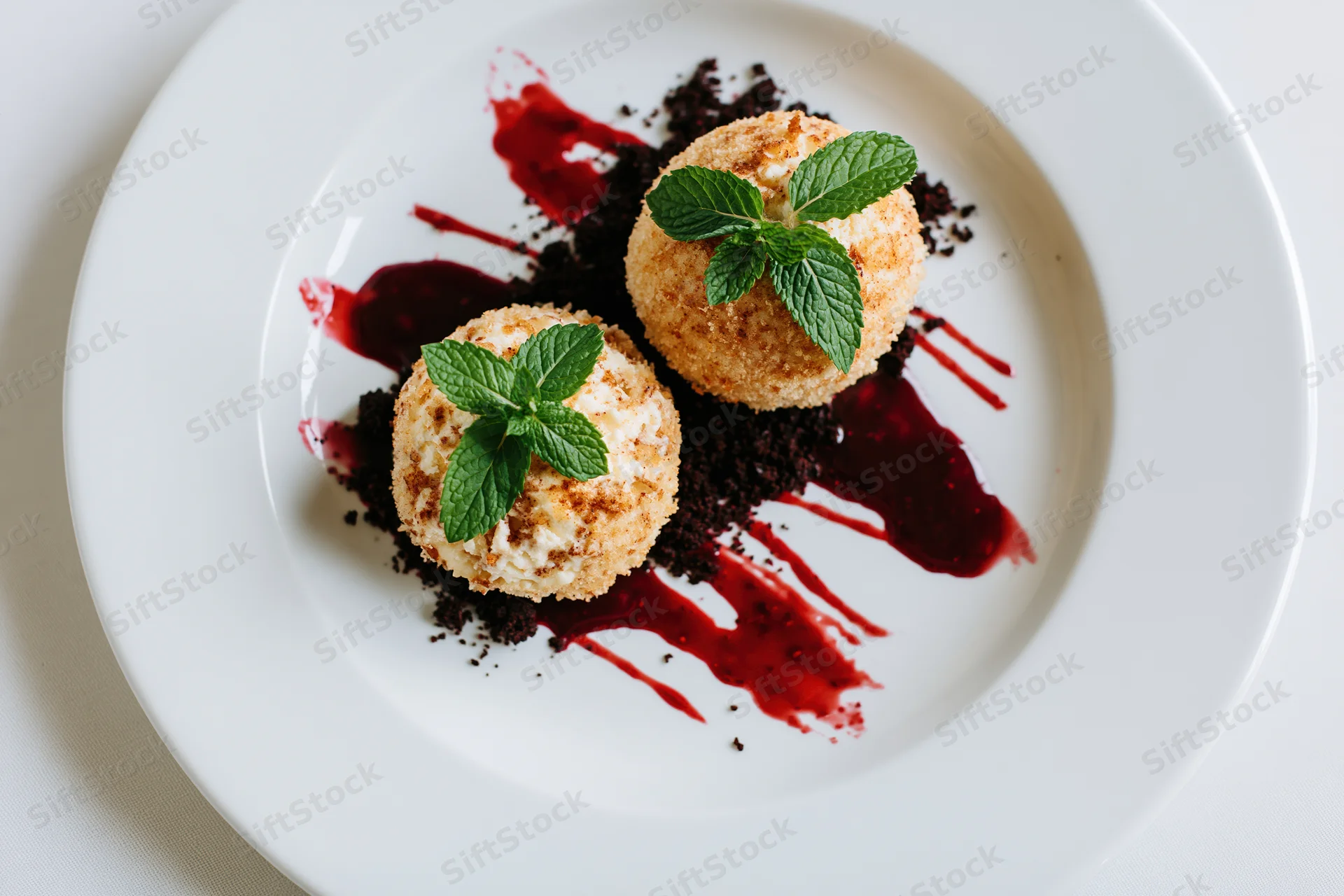 Two golden fried ice cream scoops topped with mint and red sauce on a white plate