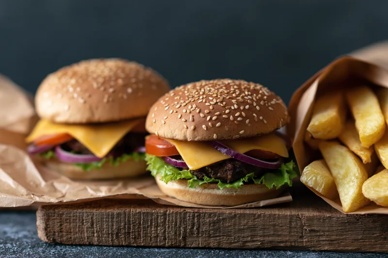 Two cheeseburgers with sesame seed buns and french fries on a wooden board