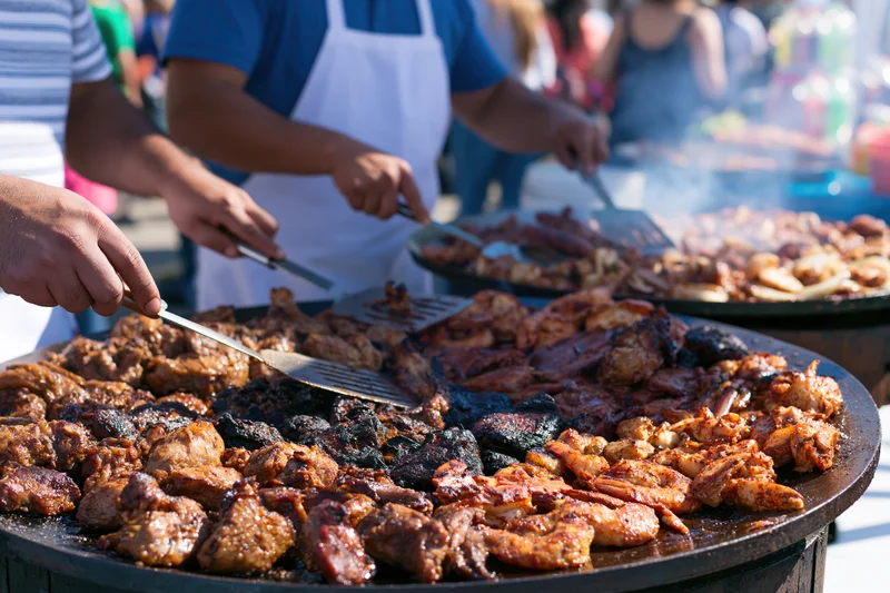 Street food vendors grilling assorted meats and seafood on large round griddles outdoors at a festival