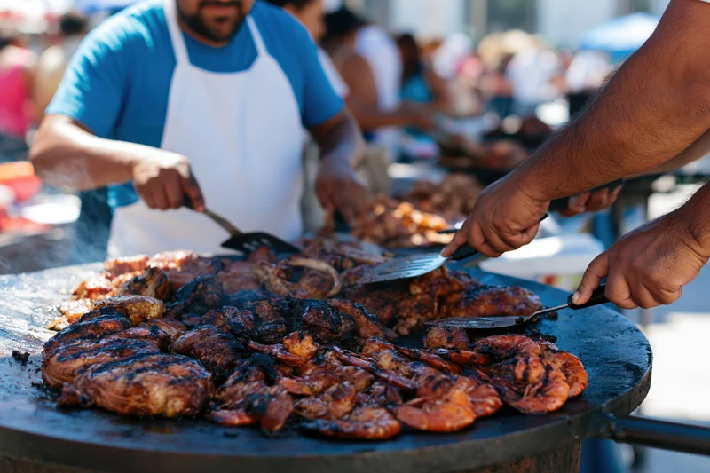 Men cooking assorted meats and seafood on a large outdoor grill at a street food market