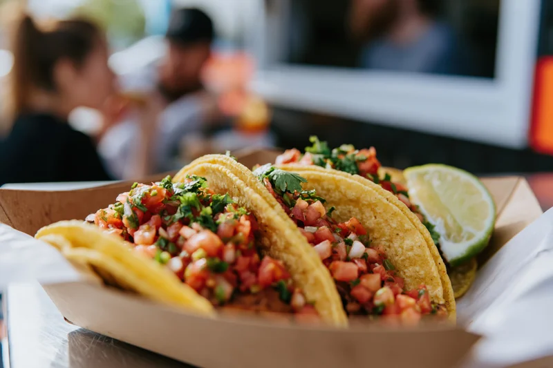 Two street tacos with pico de gallo and lime in a paper basket on a food truck counter