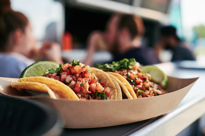 Two street tacos with shrimp and salsa in a paper basket on a food truck counter