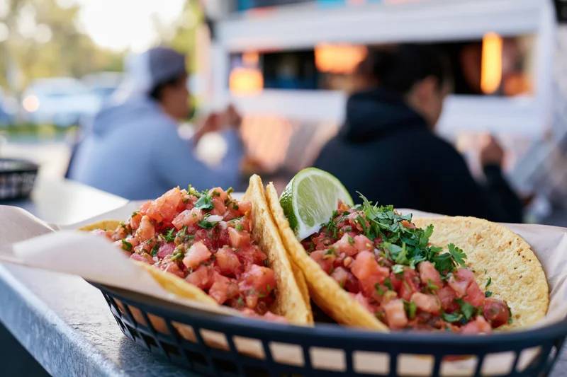 Two street tacos with salsa and lime in a paper basket on a food truck counter